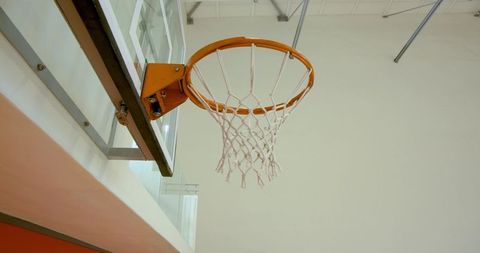 Overhead basketball hoop on glass backboard in modern gymnasium with orange rim and net
