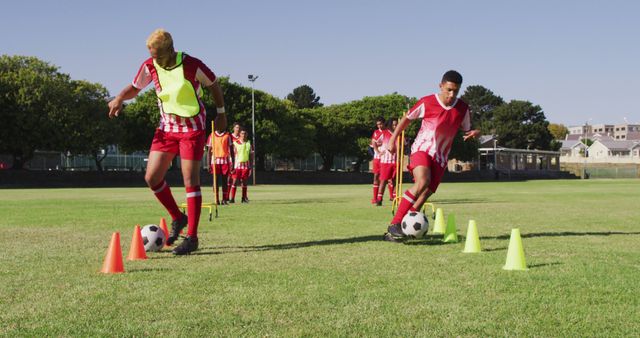 Children participating in soccer training session outdoors, practicing drills with orange and green cones. They are wearing red and white uniforms and are focused on their skills. This is useful for illustrating youth sports development, teamwork, coordination, and healthy outdoor activities.
