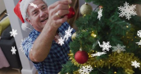 Senior Man in Santa Hat Decorating Christmas Tree with Ornaments