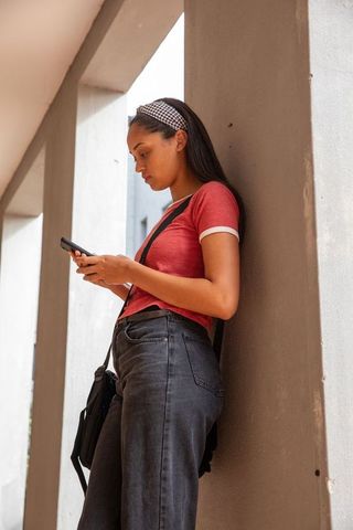 Teen girl leaning on pillar checking smartphone in urban corridor wearing red tee and headband