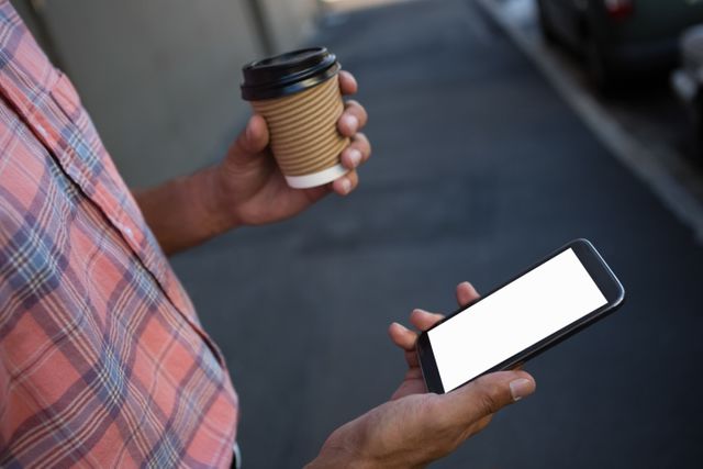 Midsection of man having coffee while using mobile phone