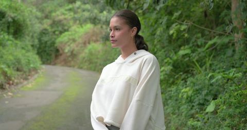 Woman standing on mossy trail wearing cream oversized hoodie, contemplative serene portrait