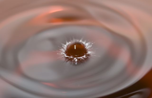 Visually stunning close-up of a water droplet impacting surface creating symmetrical ripples spreading outward. Perfect for illustrating concepts related to calmness, fluid dynamics, nature's beauty, and scientific studies. Ideal for use in water-related advertisements, educational materials, environmental awareness posters, and desktop wallpapers.