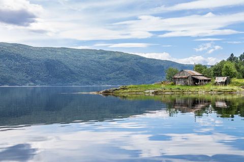 Rustic boathouse on tranquil fjord with mountain reflection and calm water