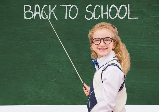 This image shows a young girl smiling and pointing at a 'Back to School' message on a green chalkboard. She is wearing glasses and a school uniform, indicating readiness for the new academic year. Ideal for use in educational materials, school promotions, back-to-school campaigns, and classroom decorations.