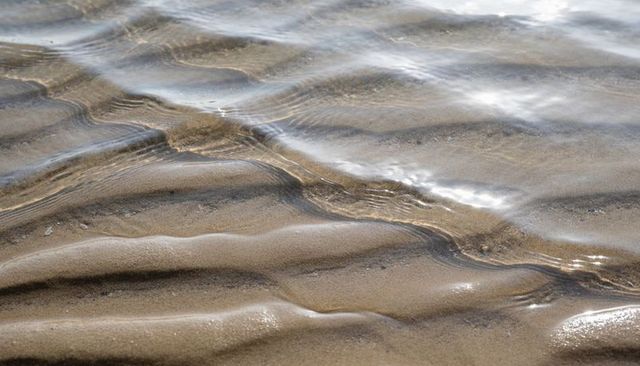 Sunlit rippling tidal sand runnels reflecting shallow seawater on quiet beach at low tide