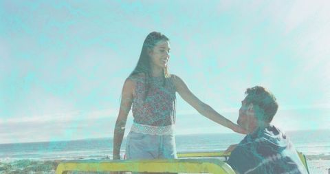Smiling woman reaching toward seated man on seaside promenade with yellow railing sunny day