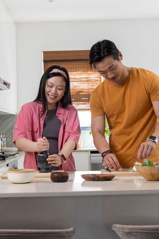 Asian couple preparing fresh meal together at bright kitchen island smiling and cooking
