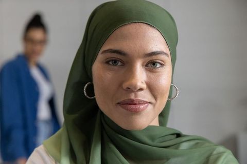 Confident young woman wearing olive hijab smiling and leading modern office team portrait