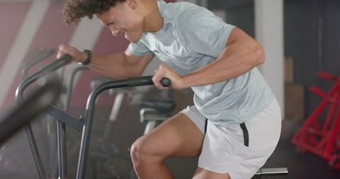 Determined Young Man Exercising on Stationary Bike in Modern Gym