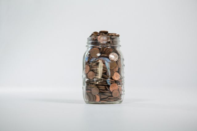 Glass jar full of coins on white background
