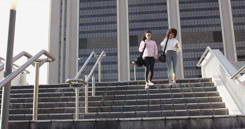 Two Women Walking Down Urban Stairs Wearing Leggings and Carrying Black Gym Bags