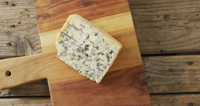Image overhead shot of wedge of blue cheese on chopping board, on rustic wooden table. quality, tasty light food snack.
