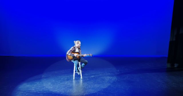 A woman delivers a focused solo guitar performance under serene blue lighting. - Download Free Stock Photos Pikwizard.com
