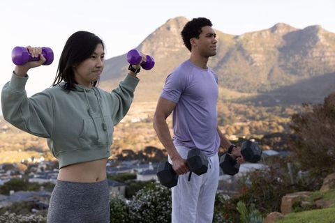 Diverse workout partners exercising outdoors with dumbbells on hillside