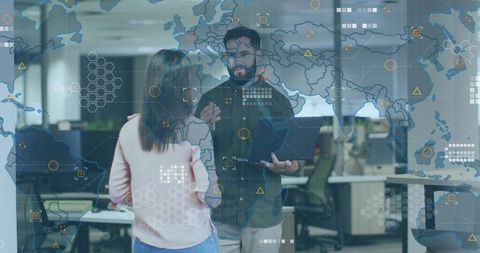Colleagues collaborating over laptop with global data HUD overlay inside modern office
