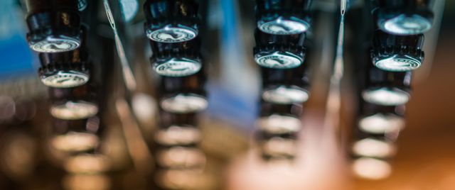 Unique abstract depiction of bottle caps arranged on rack. With a shallow depth of field and bokeh effect, this image can be ideal for brewery promotions, bar decorations, or artistic marketing materials focusing on beverages.