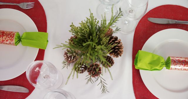 A festive table setting features red placemats, green napkins, and a centerpiece with pine cones, with copy space. The arrangement suggests a holiday meal or celebration, inviting a sense of warmth and tradition.