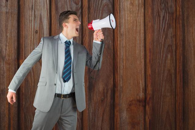 Businessman in a suit and tie shouting through a megaphone against a wooden wall. Ideal for concepts related to communication, leadership, corporate announcements, motivational speeches, and professional presentations.
