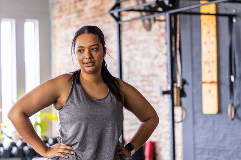 Asian woman pausing workout and catching breath in industrial gym with brick wall