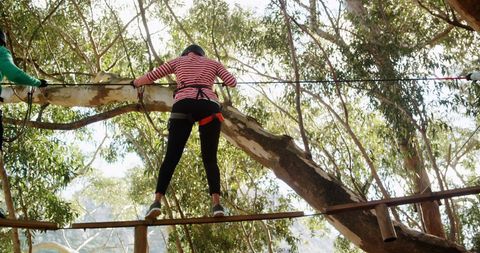 Person in striped shirt navigating a ropes course amidst trees, perfect for illustrating concepts of teamwork, outdoor challenges, personal growth, and adventure tourism. Ideal for adventure-related promotions or educational materials about overcoming fears.