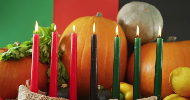 Seven Kwanzaa candles are lit, arranged in a Kinara with pumpkins and assorted vegetables surrounding them. This scene symbolizes the celebration of Kwanzaa, a festive and cultural tradition focusing on unity and community. Perfect for illustrative use in articles or materials about holiday traditions, cultural events, and Kwanzaa-specific celebrations.