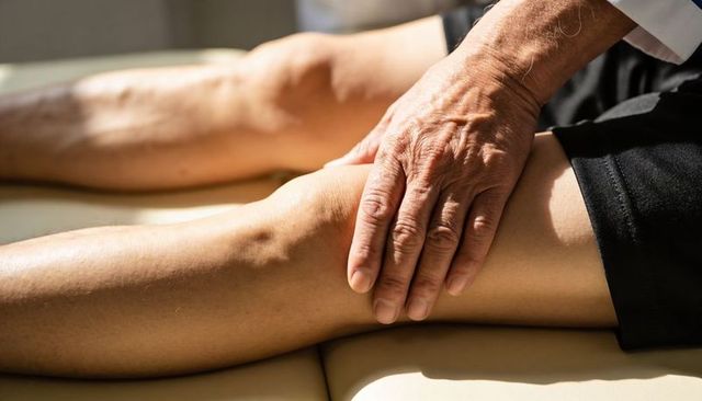 Therapist hands examining knee of older adult during physical therapy session, close-up