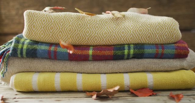 Image of folded blankets and autumn leaves on wooden background. seasons, autumn, fashion, relax and coziness concept.