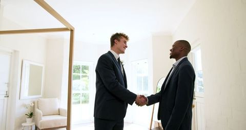 Groom and best man shaking hands in bright room