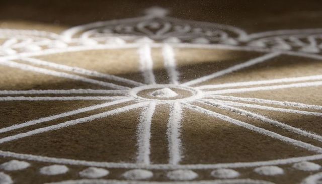 White powder mandala radial floor design on rustic brown porch with geometric spokes