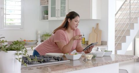 Plus Size Biracial Woman Preparing Meal in Modern Kitchen with Tablet