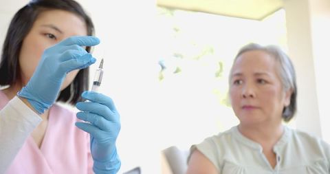 Nurse Preparing Syringe with Senior Asian Woman Observing Attentively