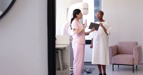 Nurse explaining mammogram procedure with tablet while patient preparing for screening