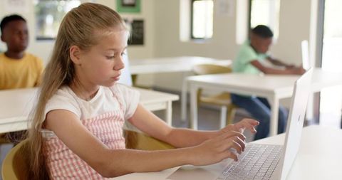 Schoolgirl Typing on Laptop in Bright Classroom with Diverse Classmates Learning