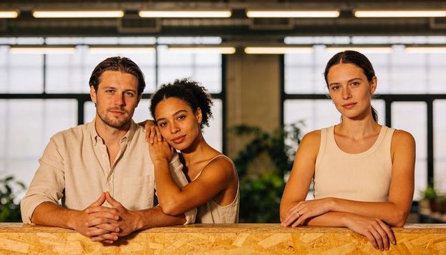 Three-person team leaning on osb counter in modern coworking space showing collaboration