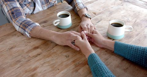 Couple Holding Hands Over Coffee at Cozy Wooden Table