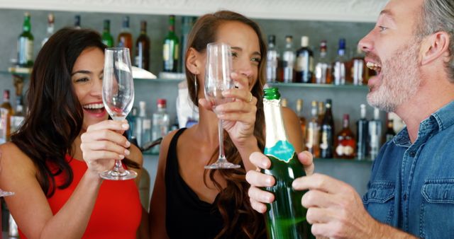 Young women holding champagne flute while man opening bottle of champagne in restaurant 