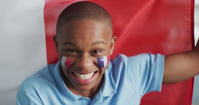 Teenager joyfully cheering with French flag painted on face, showcasing patriotism and excitement. Perfect for use in promotions, advertisements, or articles focusing on sports events, national pride, or youthful enthusiasm.