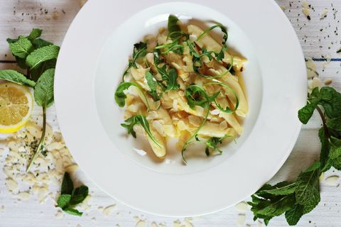 Serving lemon almond pasta with arugula and fresh mint on white plate