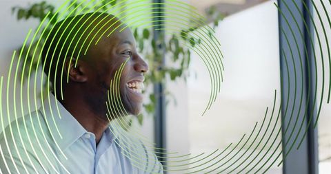Smiling black professional looking out window with green concentric graphic, bright office