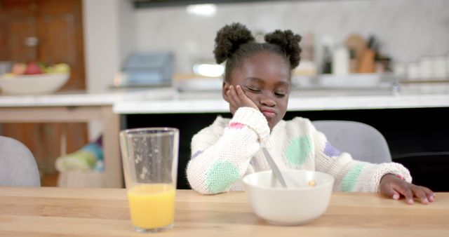 Bored african american girl having breakfast and sitting at table at home. Childhood, food and domestic life, unaltered.