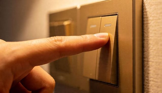 Index Finger Pressing Bronze Rocker Light Switch under Warm Amber Ambient Lighting