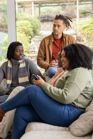 Diverse friends chatting and relaxing on sofa in bright sunroom with garden view