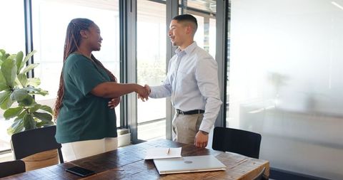 Diverse business partnership: woman shaking hands with businessman in office