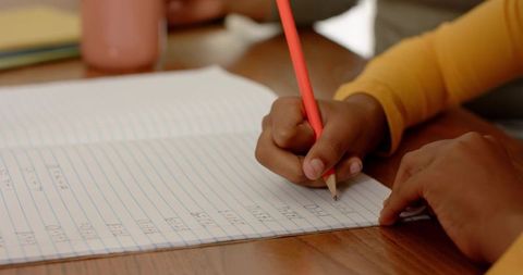 Young Student Practicing Handwriting While Teacher Guides Pencil on Wide-Ruled Notebook
