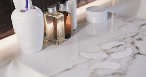 Under-eye patches lining marble vanity with skincare bottles and toothbrush
