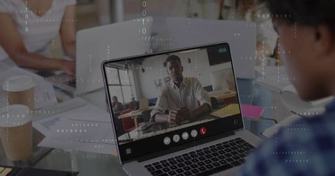 Hybrid team collaborating with remote participant via video call on laptop in modern office