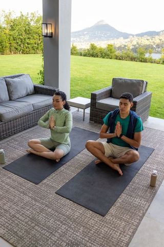 Couple meditating on patio practicing mindfulness and yoga in sunlit backyard with scenic view