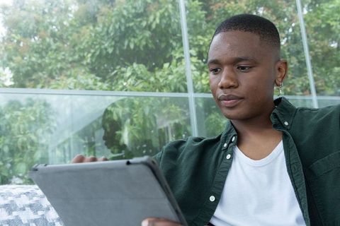 African american man using tablet in sunroom with glass panels and greenery