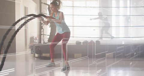 Woman swinging battle ropes in boxing ring gym for high-intensity functional training
